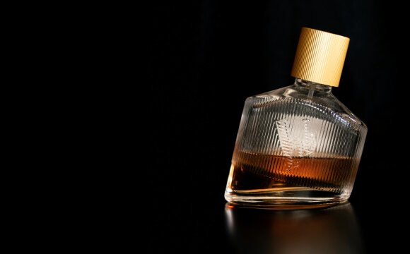 Arany kupakos üvegparfüm sötét háttér előtt.