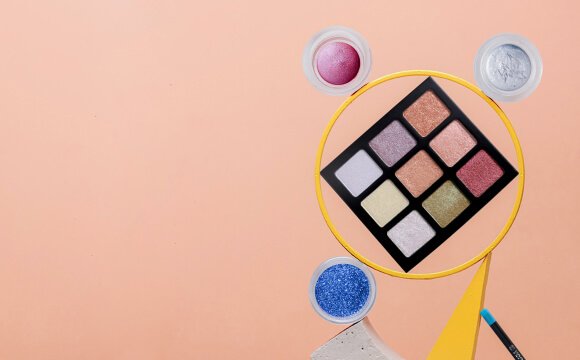 Szemhéjpúder paletta és csillámok halvány rózsaszín háttéren.