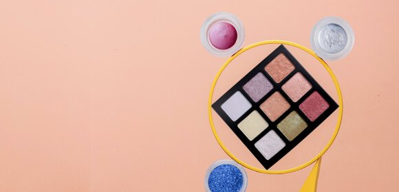 Színes szemhéjpúder paletta és különböző árnyalatú púderek rózsaszín háttéren.