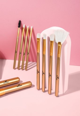Aranyszínű sminkecsetek készlet rózsaszín háttér előtt.